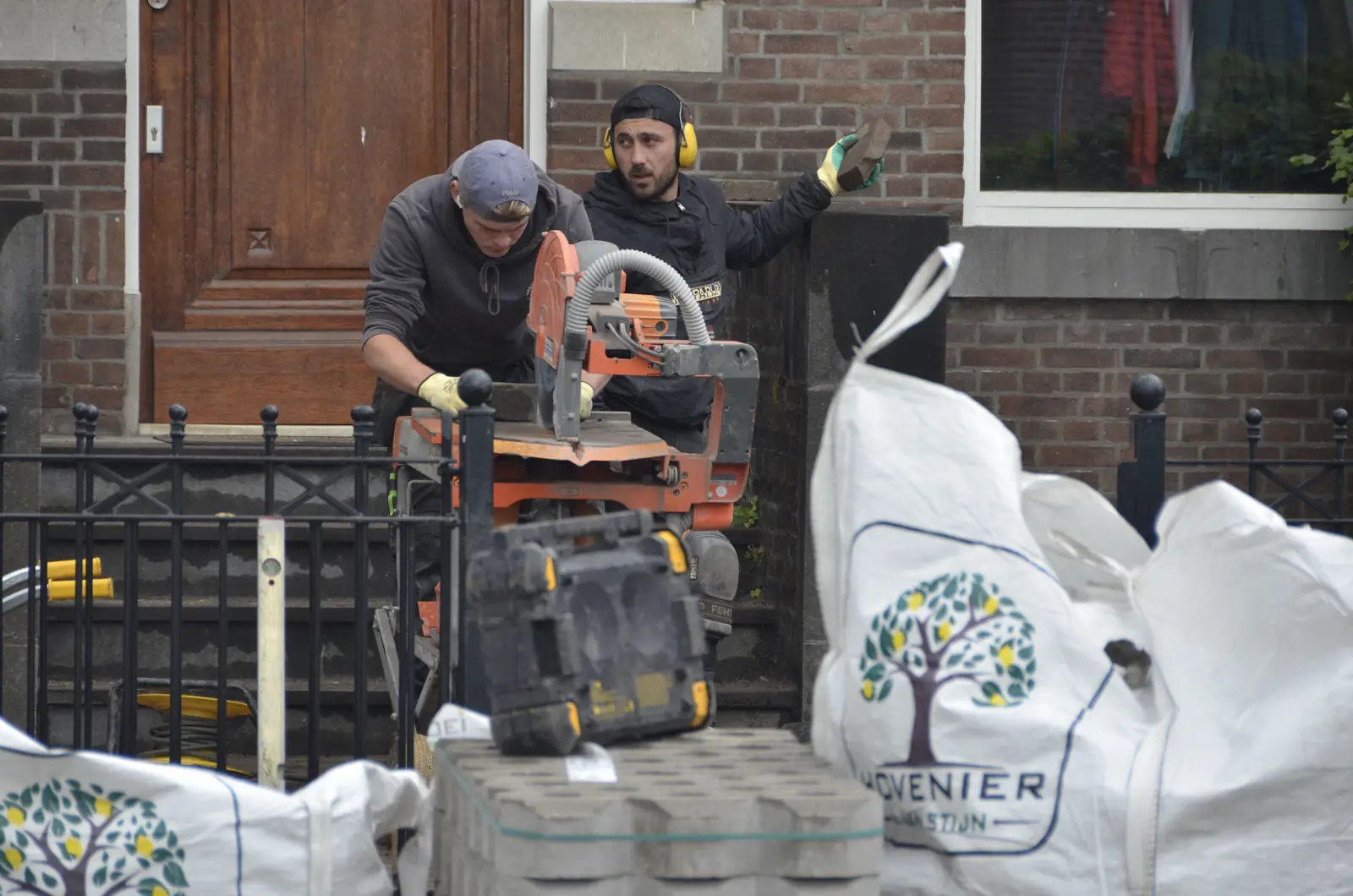 Twee hoveniers zagen stenen op maat, naast big bags met ons logo — Rotterdam-Hillegersberg